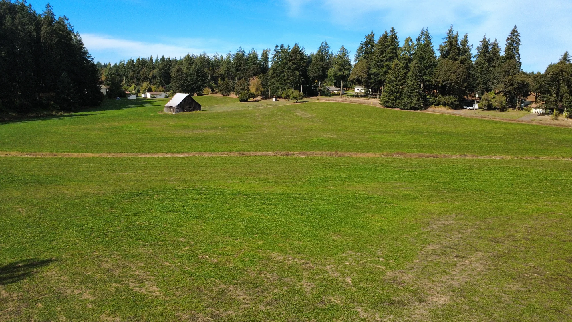 Aerial photograph of an open grassy field with a small old barn and surrounding trees